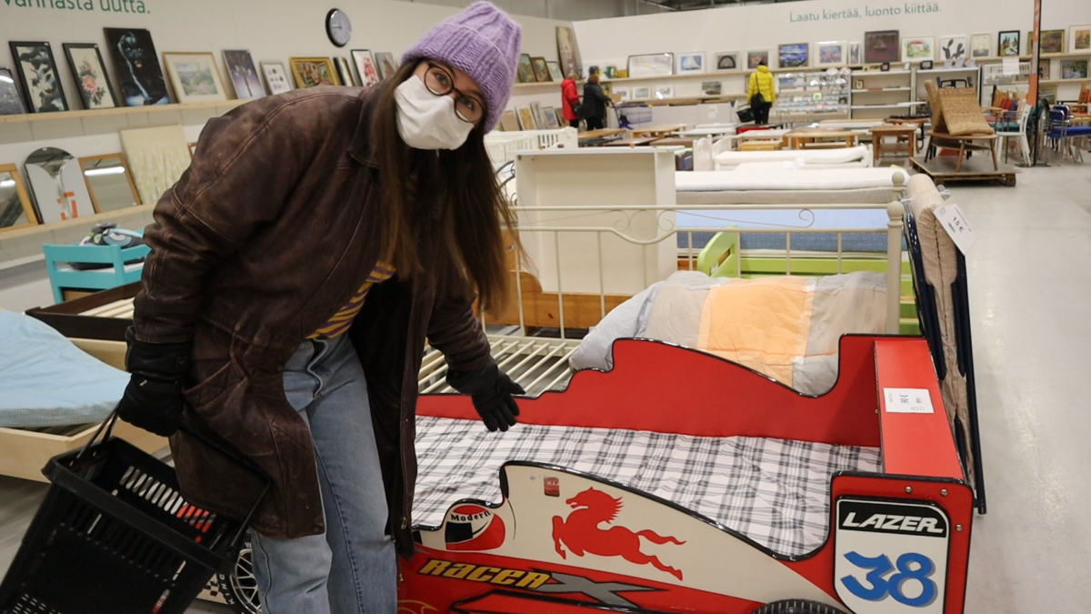 Kvinna med munskydd böjer sig ned och visar en säng som ser ut som en ferrari. 