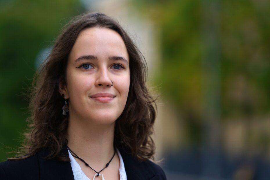 Anna Louhisto i närbild. Hon tittar in i kameran med ett avslappnat ansiktsuttryck. Bakgrunden är suddig och grön.