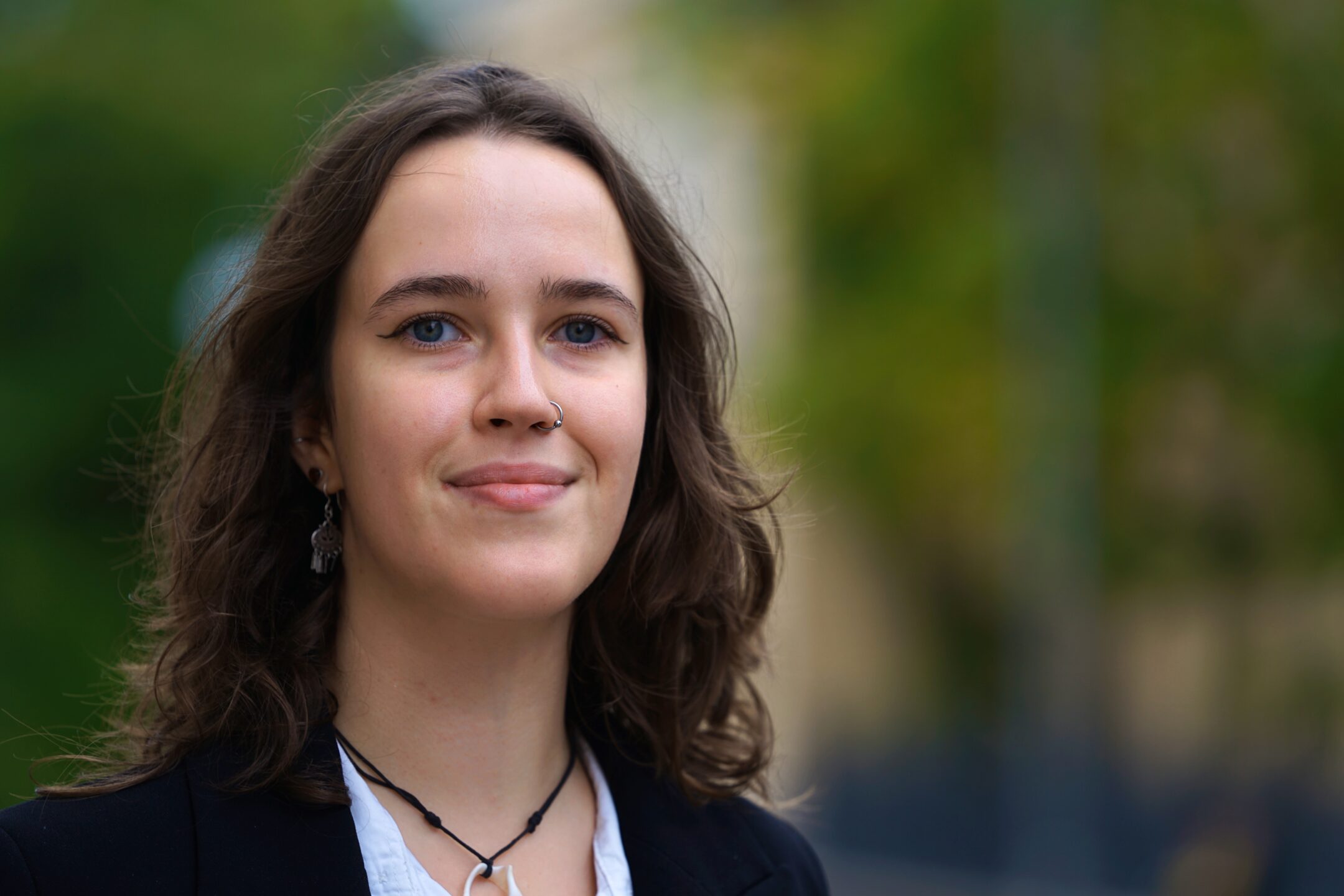 Anna Louhisto i närbild. Hon tittar in i kameran med ett avslappnat ansiktsuttryck. Bakgrunden är suddig och grön.