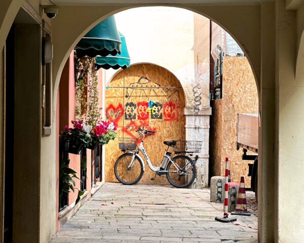 En rundad portöppning. I bakgrunden en rundad trädörr med graffitikonst. Framför den står en parkerad cykel.