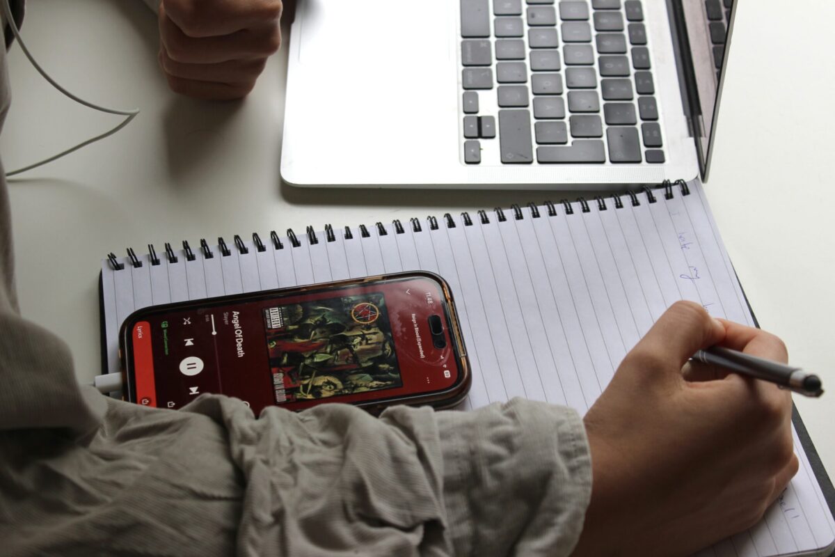 En hand som skriver i ett häfte. På häftet en telefon som visar att låten Angel of Death av Slayers spelar.