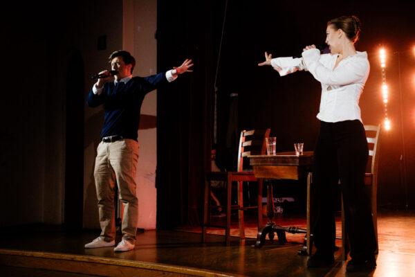 Två skådespelare står på scen. De sjunger i mikrofon och sträcker ut sina händer mot varandra.