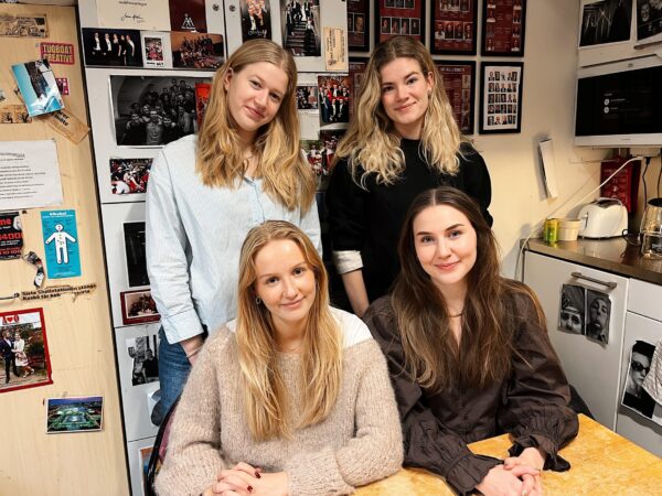 Fyra personer sitter i ett kafferum och ler in i kameran.