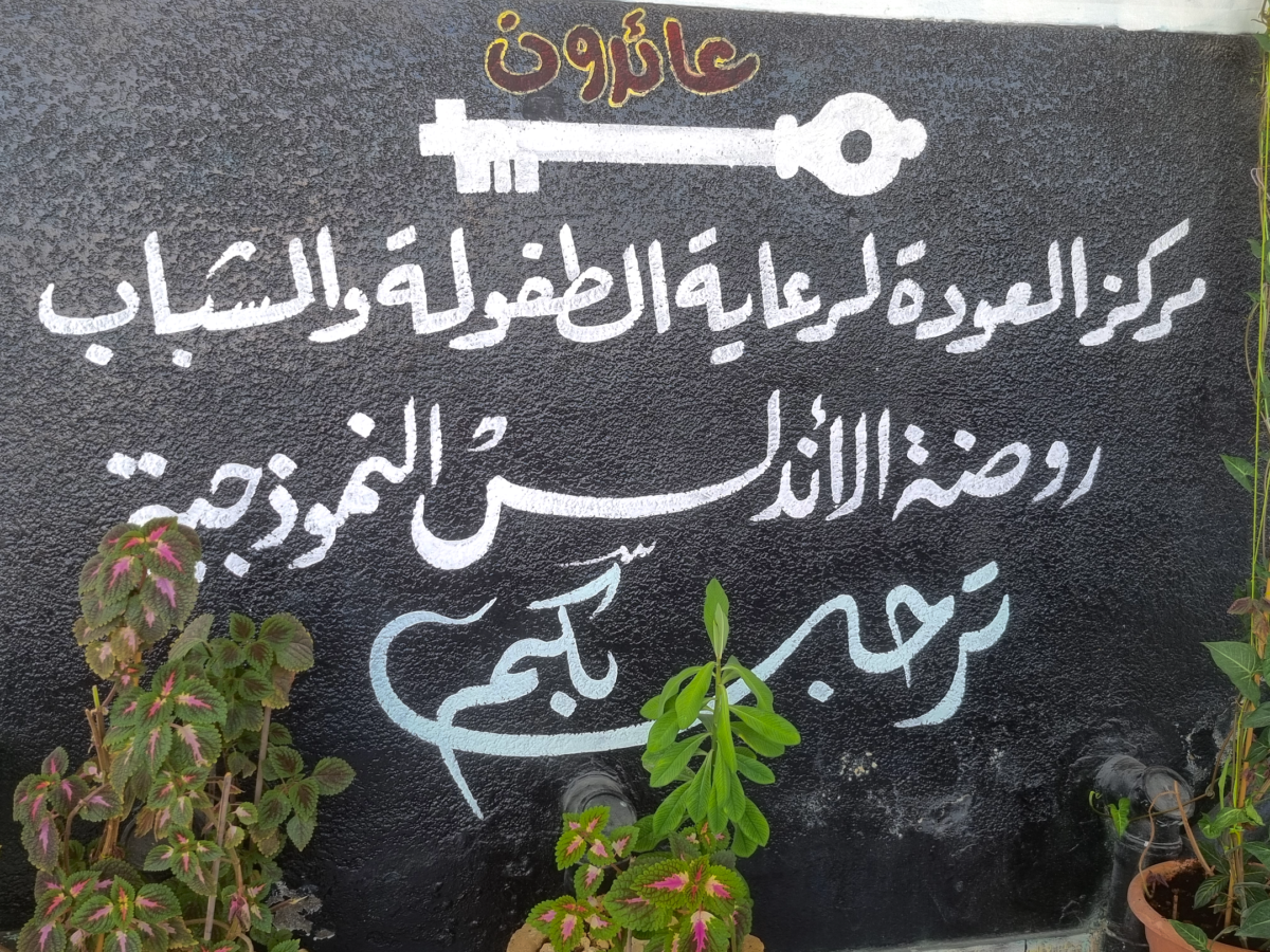 En vit målad text på en grå vägg. Texten är på arabiska. Ovanför den är en nyckel målad i samma vita färg.