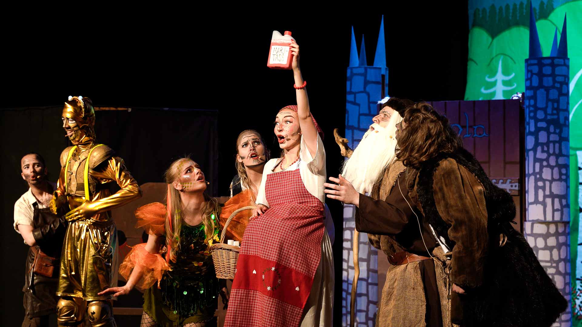 Jungfru Marjatta håller en flaska alkohol ovanför huvudet. De andra skådespelarna tittar förskräckt på henne.