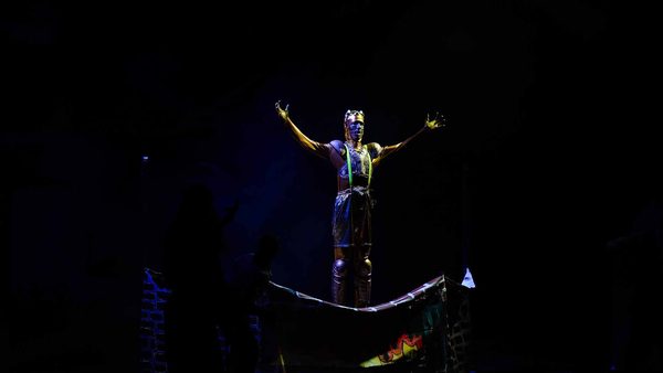 Kvarnen Sampo står på en piedestal i mörkret med armarna utrsträckta.