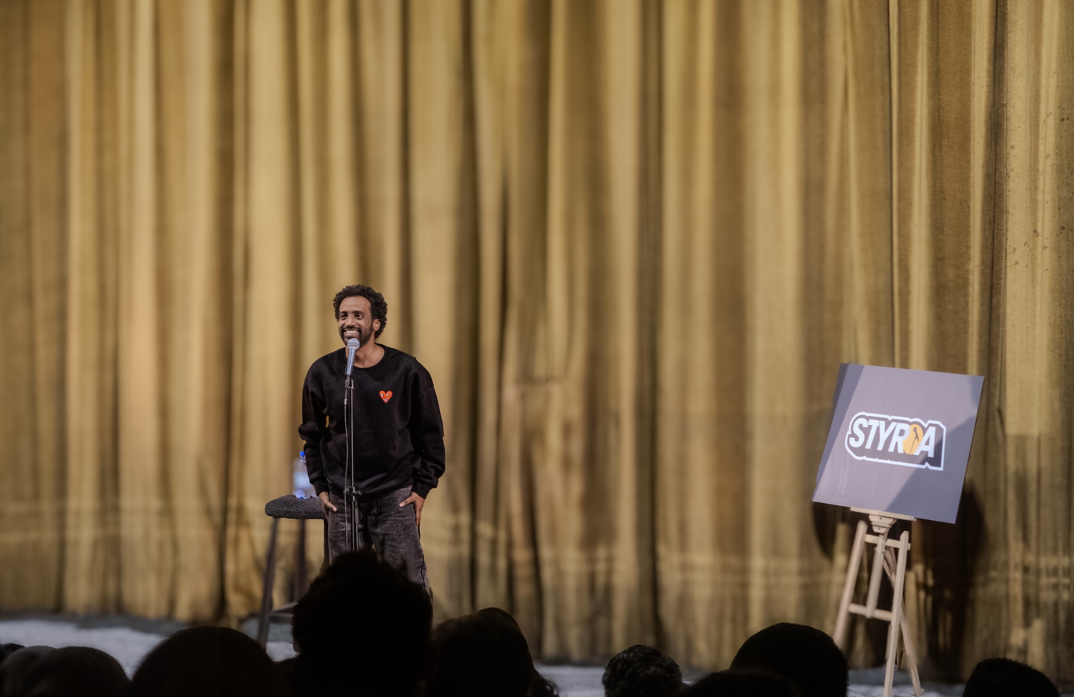 Ahmad Fadel står på en scen bredvid ett lila plakat med texten "Styria"