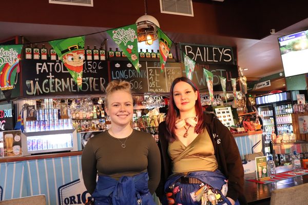 Henriikka Syrjä och Mila Jääskelä klädda i sina lila studentoveraller på en pub.