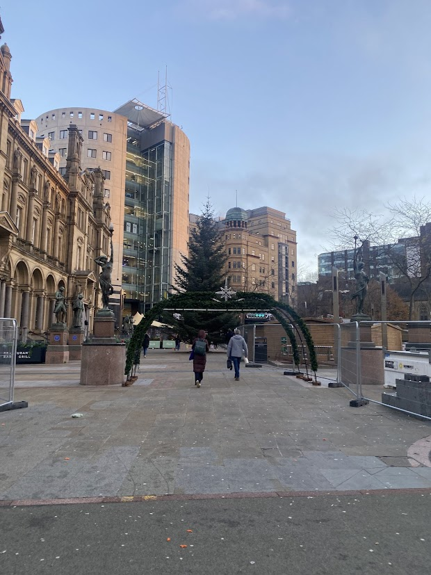 En gata i Leeds. Det är en solig dag och ingen snö syns till, men mitt på gatan står en julgransbåge med en stjärnlampa på toppen.