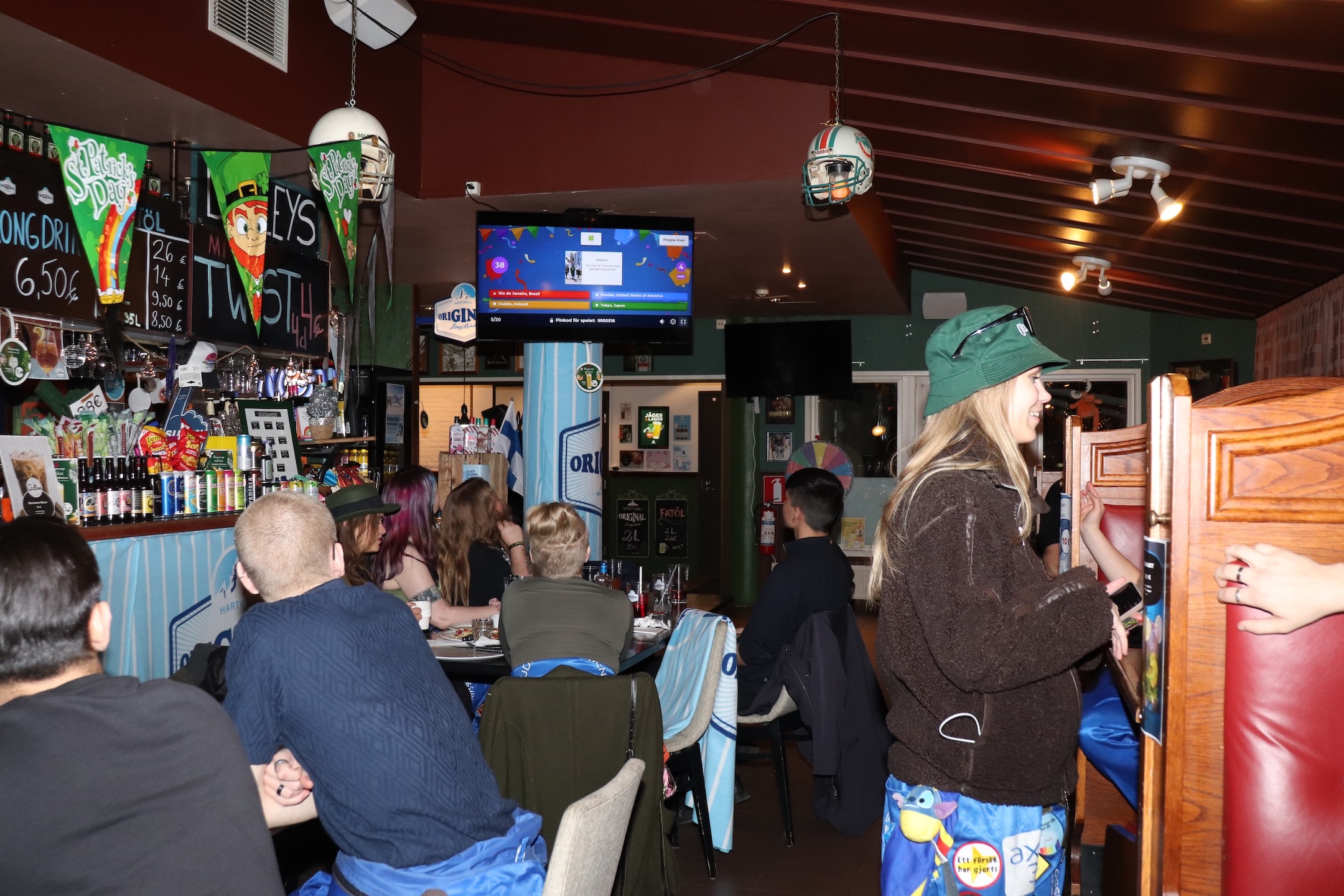 En bar full med studerande klädda i lila halare. I bakgrunden syns ett Kahoot-quiz på en tv-skärm.