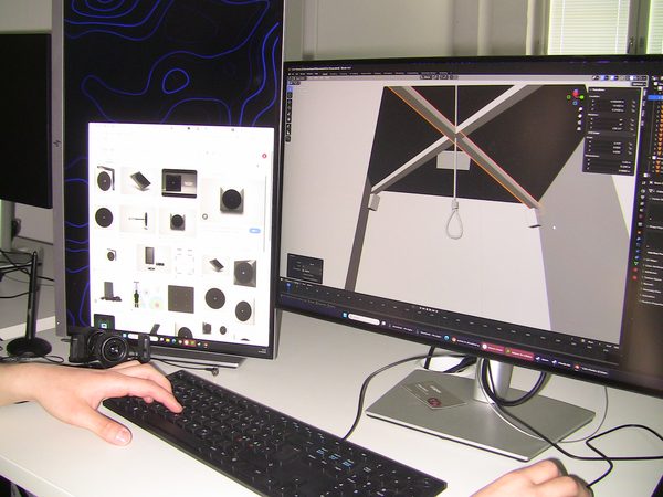 En datorskärm med en 3D-illustration av ett rum. I taket hänger en snara. Bredvid den skärmen står en annan datorskärm. Den visar olika högtalare.